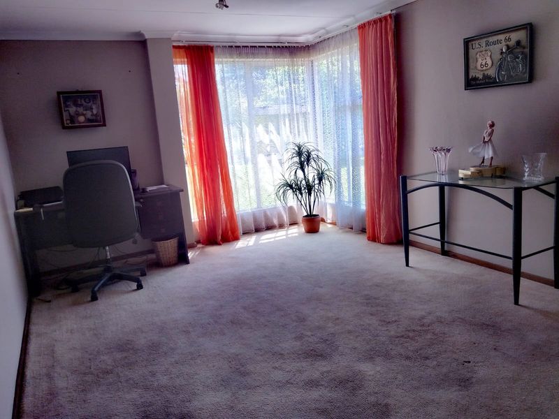 A living room featuring a large bay window with natural light, coved ceilings, and carpeted flooring, offering a comfortable and versatile living space.