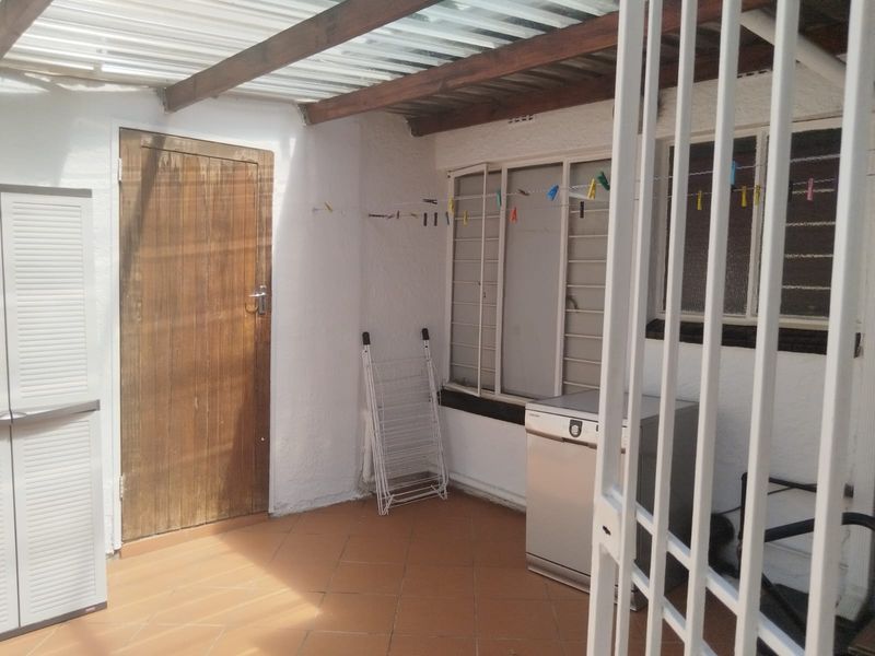 A functional outdoor laundry area featuring tiled flooring, a covered roof structure with timber beams, and secure access.