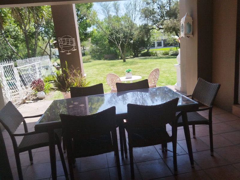 A covered outdoor patio area featuring tiled flooring and support columns, overlooking a spacious green garden.