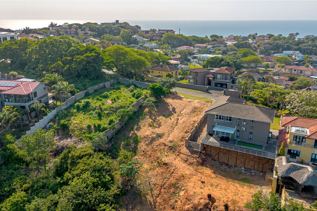 Aerial view of a vacant residential plot situated in a developed neighborhood, featuring established boundary walls and proximity to coastal views.