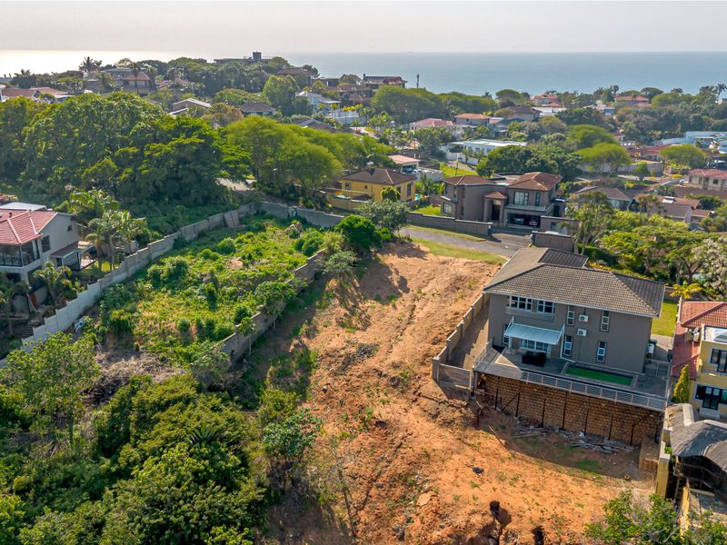 Aerial view of a vacant residential plot situated in a developed neighborhood, featuring established boundary walls and proximity to coastal views.