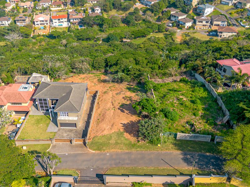 Aerial view of a vacant residential plot situated in a developed suburban neighborhood, featuring established boundary fencing and access to a paved street.