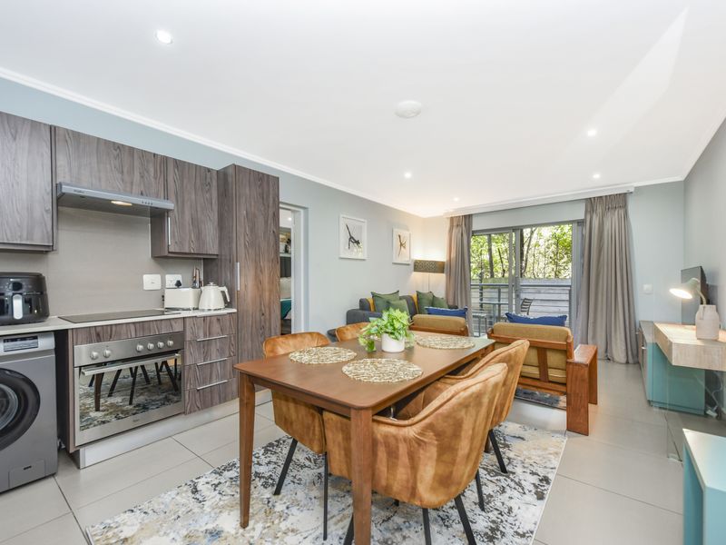 Modern open-plan living area featuring a well-equipped kitchen with wood-grain cabinetry, integrated appliances, and seamless flow to a private balcony through sliding glass doors.