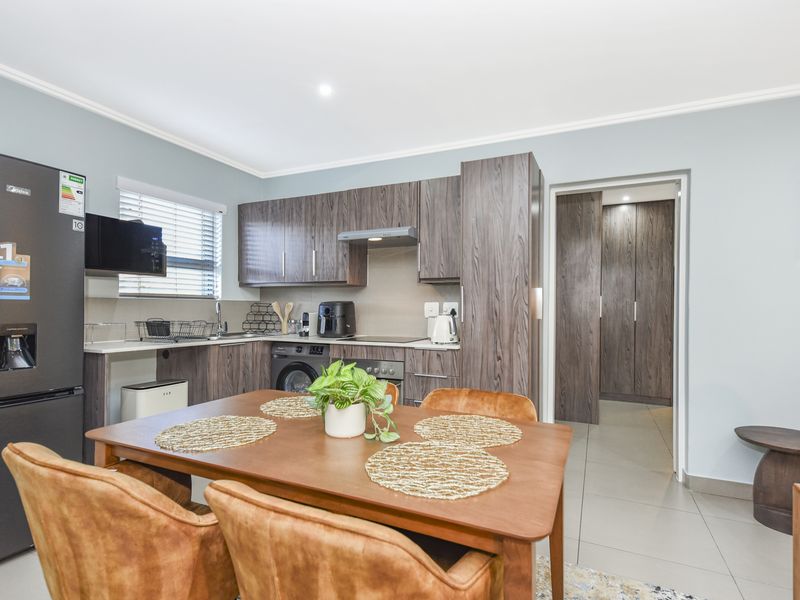 Modern open-plan kitchen featuring dark wood cabinetry, integrated appliances, and tiled flooring, seamlessly flowing into the dining area with access to adjacent storage.