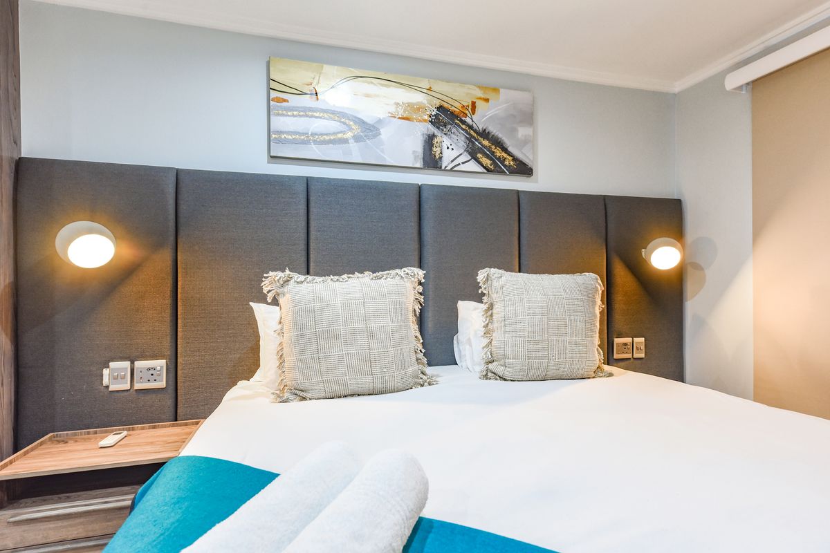 A well-appointed bedroom featuring a modern upholstered headboard, integrated wall-mounted reading lights, and convenient built-in bedside shelving with electrical points.