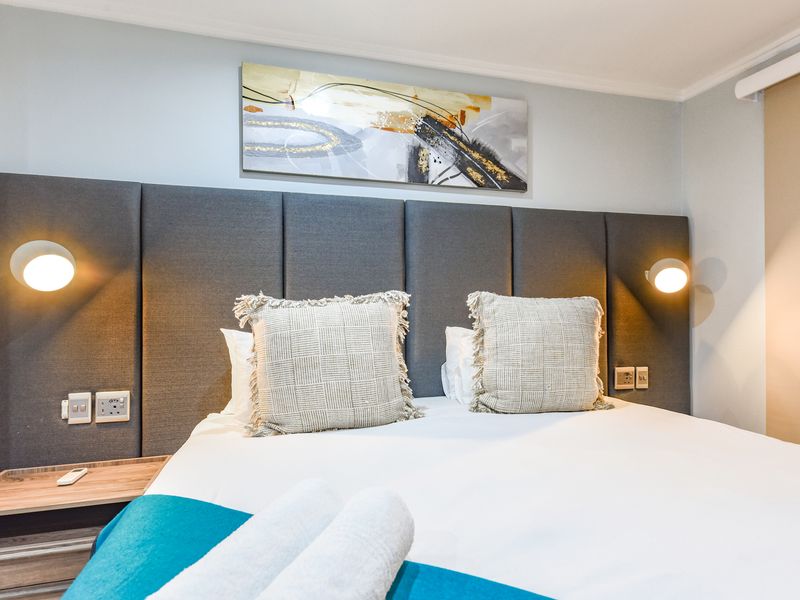A well-appointed bedroom featuring a modern upholstered headboard, integrated wall-mounted reading lights, and convenient built-in bedside shelving with electrical points.