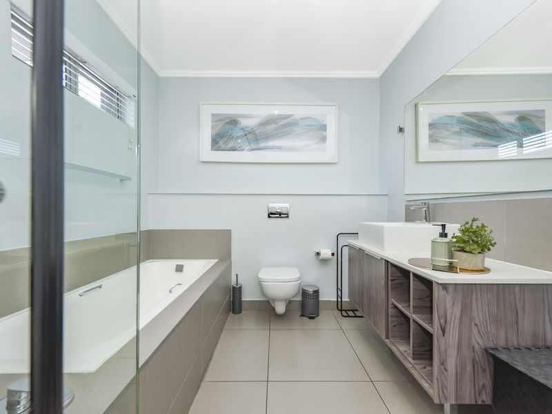 Modern bathroom featuring a wall-hung toilet, vessel sink vanity, large wall mirror, and a built-in bathtub with a glass shower screen.