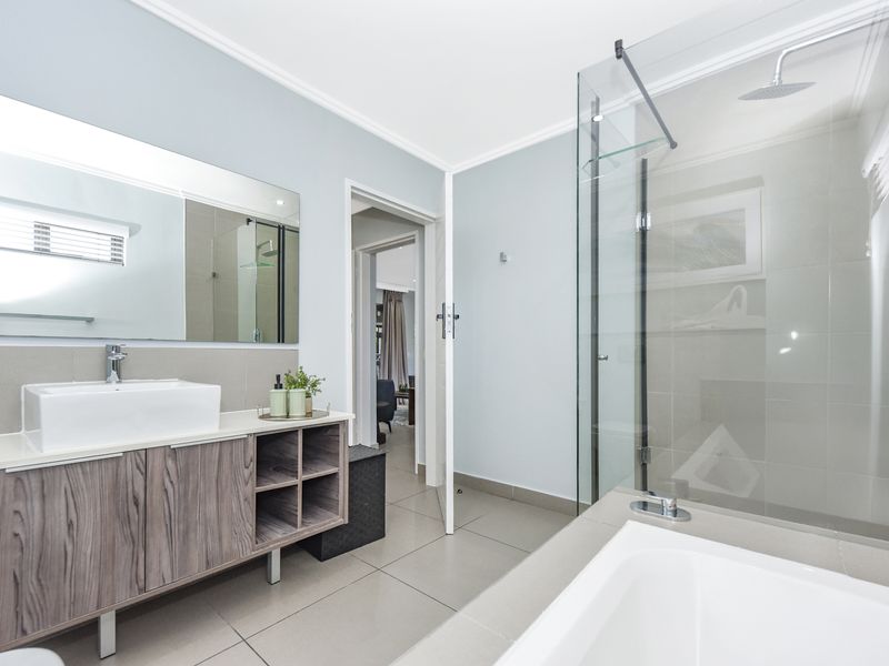 Modern bathroom featuring a wood-finish vanity with vessel sink, a glass-enclosed shower, and a separate built-in bathtub with neutral tile flooring.