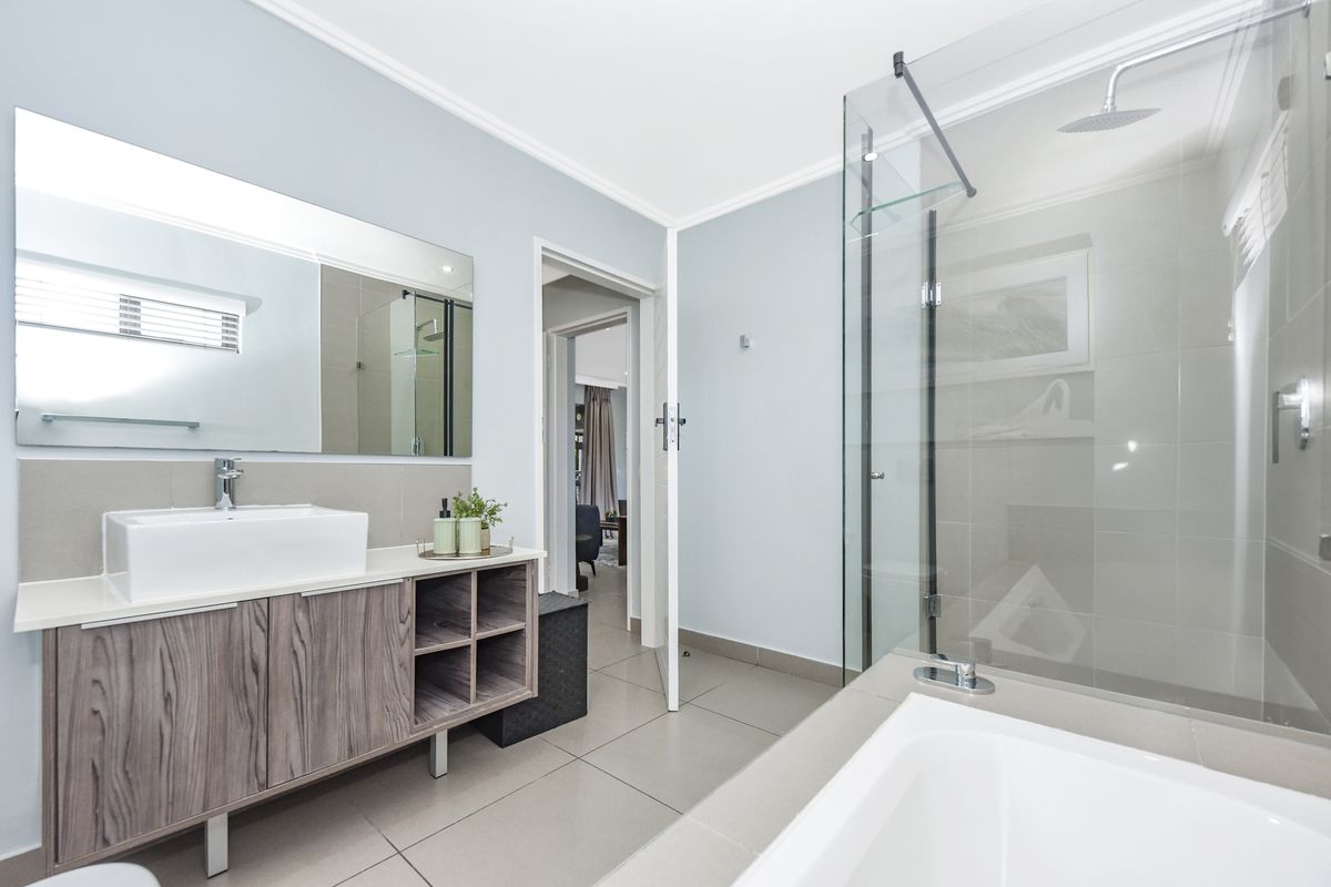 Modern bathroom featuring a wood-finish vanity with vessel sink, a glass-enclosed shower, and a separate built-in bathtub with neutral tile flooring.