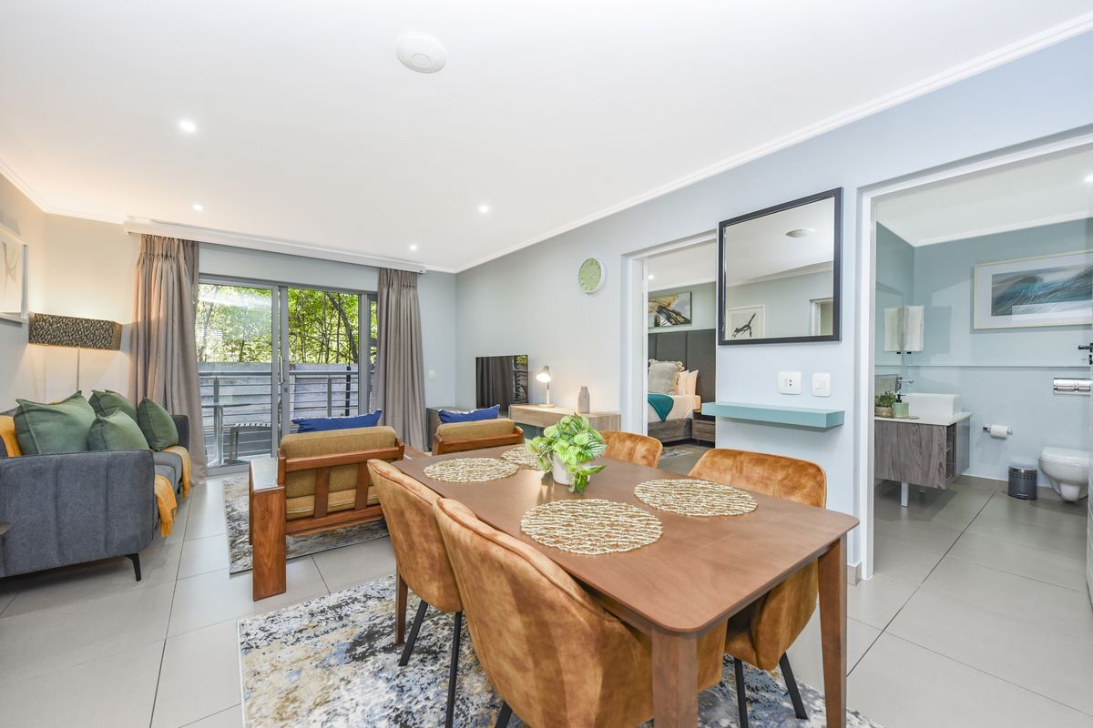 A bright open-plan living and dining area featuring tiled floors, recessed lighting, and direct access to a balcony through sliding glass doors.