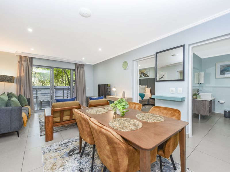 A bright open-plan living and dining area featuring tiled floors, recessed lighting, and direct access to a balcony through sliding glass doors.
