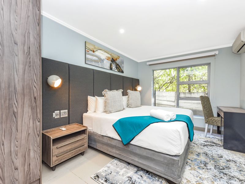 A well-maintained bedroom featuring a built-in wardrobe, upholstered headboard with integrated lighting, and a split-system air conditioner.