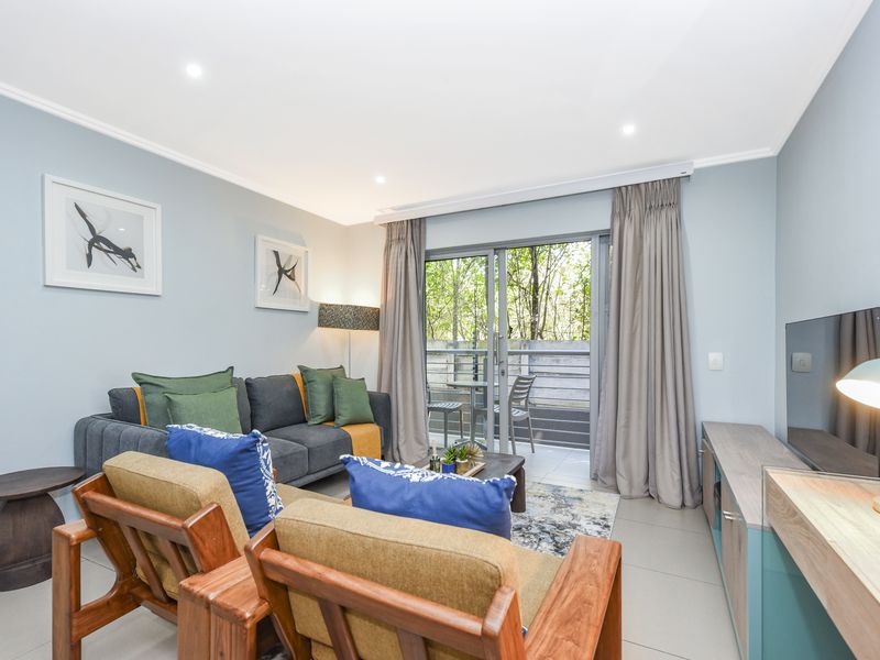 A well-maintained living room featuring tiled flooring, recessed lighting, and a sliding glass door providing access to an outdoor balcony area.