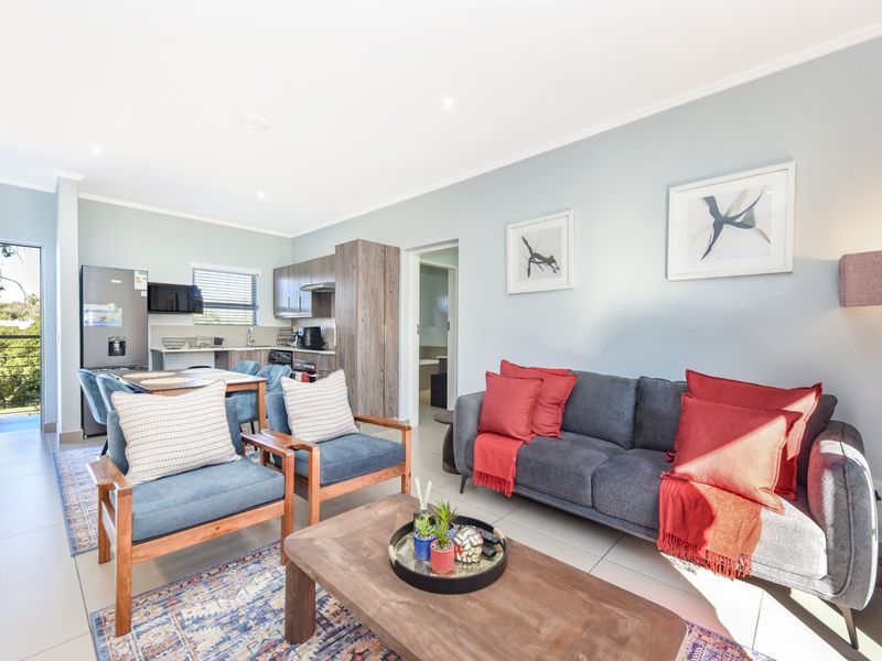 Bright open-plan living area featuring tiled floors, recessed lighting, and a compact kitchen with modern cabinetry, leading directly to an outdoor balcony.