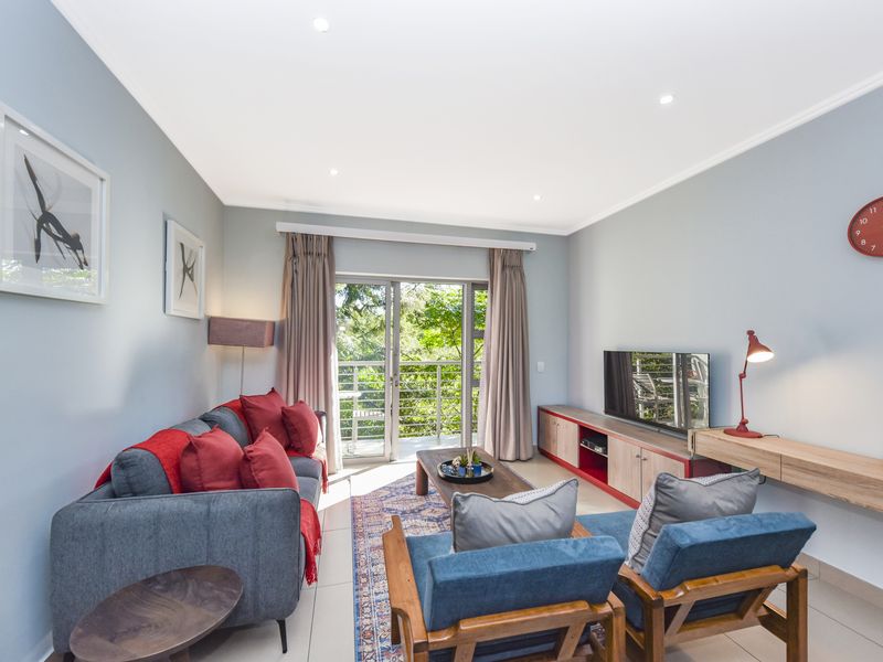 A bright and well-maintained living room featuring tiled floors, recessed lighting, and a sliding glass door providing access to a balcony.