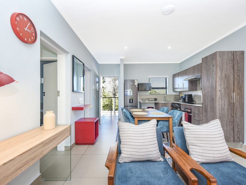 An open-plan living and kitchen area featuring modern wood-finish cabinetry, tiled flooring, and direct access to an outdoor balcony.
