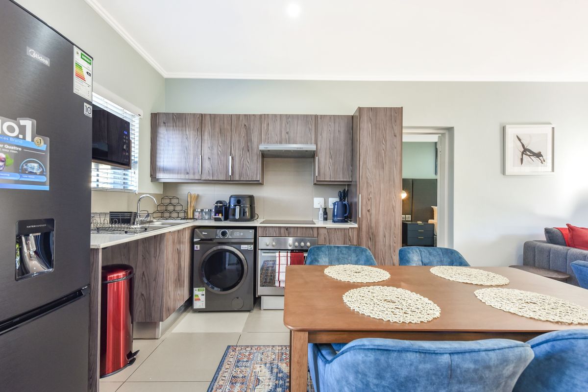 Modern open-plan kitchen featuring wood-grain cabinetry, integrated appliances, and tiled flooring, seamlessly flowing into the dining and living areas.