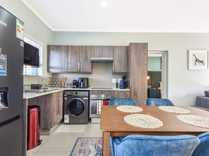 Modern open-plan kitchen featuring wood-grain cabinetry, integrated appliances, and tiled flooring, seamlessly flowing into the dining and living areas.