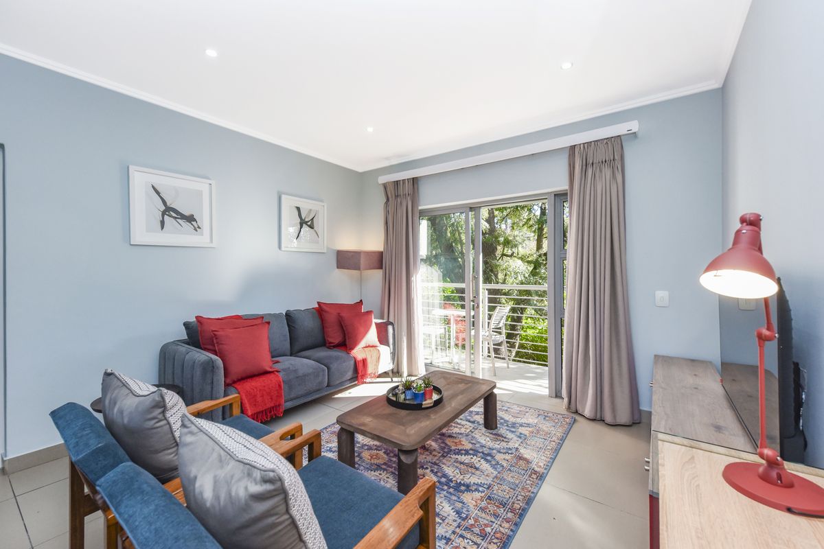 A bright and well-maintained living room featuring tiled flooring, recessed downlights, and a sliding glass door providing access to an outdoor balcony area.