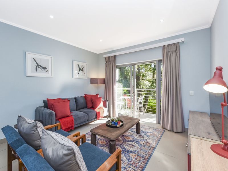 A bright and well-maintained living room featuring tiled flooring, recessed downlights, and a sliding glass door providing access to an outdoor balcony area.