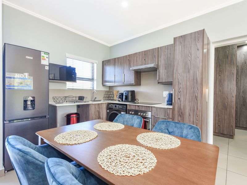 Modern open-plan kitchen featuring wood-grain cabinetry, integrated appliances, and tiled flooring, seamlessly flowing into the dining area.