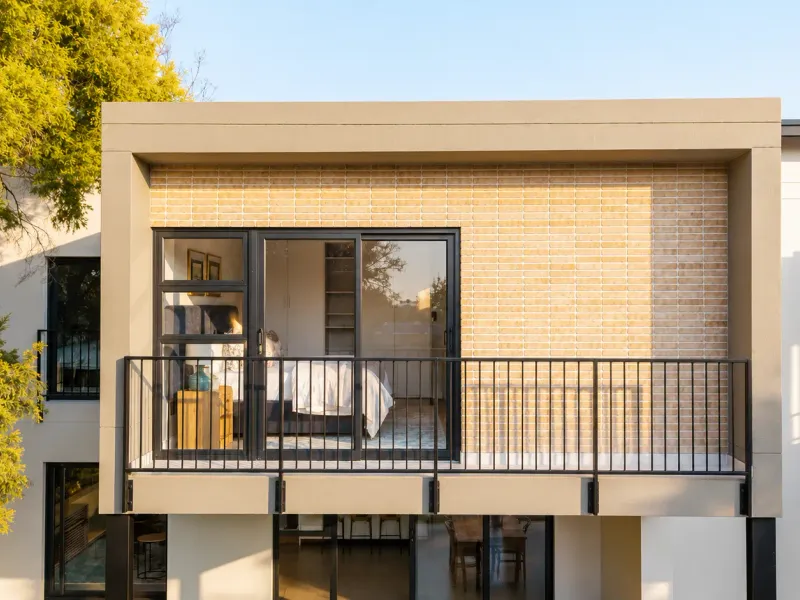A modern upper-level balcony featuring a sleek metal balustrade, sliding glass doors, and contemporary brick and concrete architectural detailing.