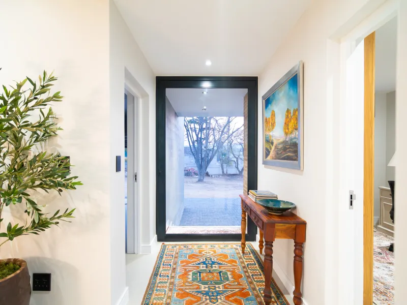 A bright and modern entrance hallway featuring clean white walls, tiled flooring, and a large glass door providing a clear view to the exterior.
