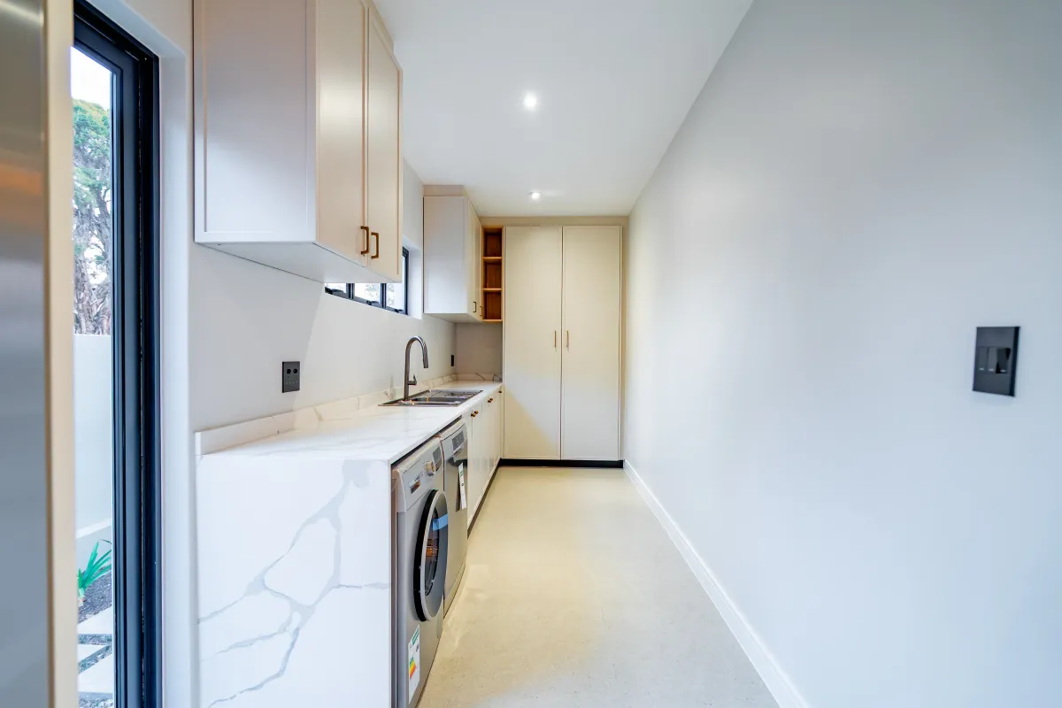 A modern, well-lit laundry room featuring sleek built-in cabinetry, stone countertops, and an integrated sink, offering a clean and functional utility space.