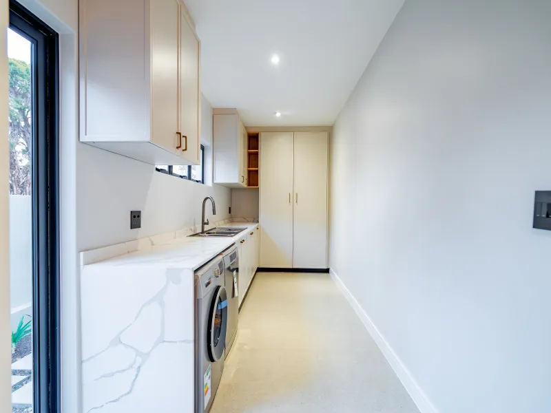A modern, well-lit laundry room featuring sleek built-in cabinetry, stone countertops, and an integrated sink, offering a clean and functional utility space.