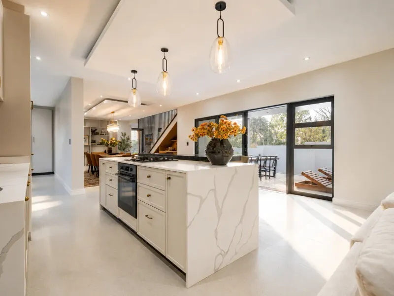Modern open-plan kitchen featuring a large stone-topped island, built-in appliances, and seamless flow to an outdoor patio area through large sliding glass doors.