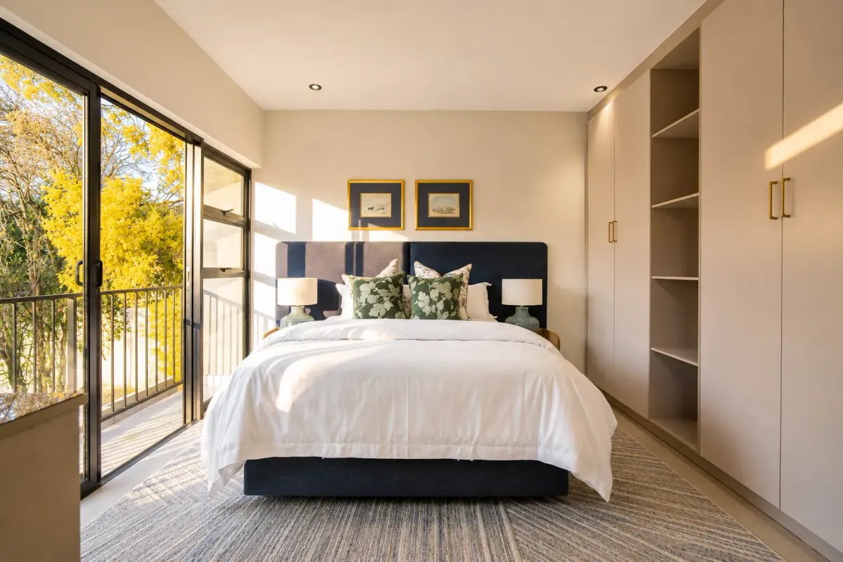 A well-maintained bedroom featuring built-in cupboards, recessed lighting, and large sliding glass doors opening onto a private balcony.
