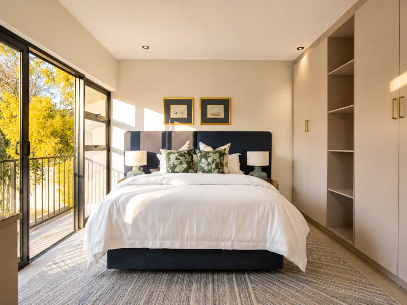 A well-maintained bedroom featuring built-in cupboards, recessed lighting, and large sliding glass doors opening onto a private balcony.