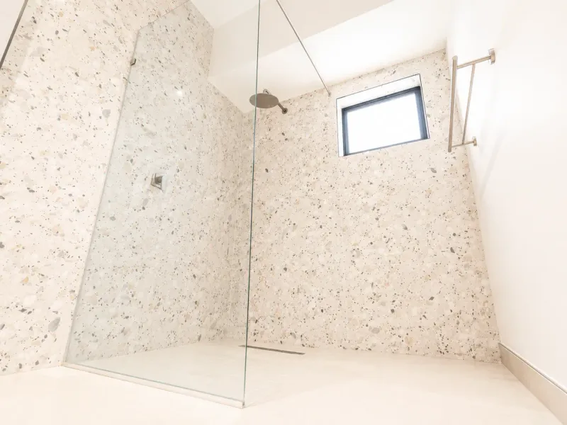 Modern walk-in shower featuring stylish terrazzo wall tiles, a frameless glass screen, a rain shower head, and a sleek heated towel rail.