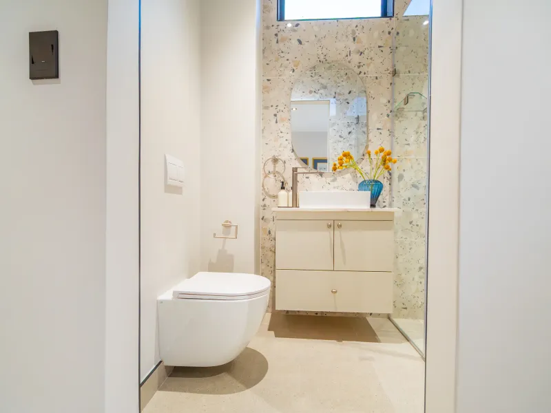 Modern bathroom featuring a wall-mounted toilet, floating vanity with vessel sink, and stylish terrazzo wall tiles with a glass shower enclosure.