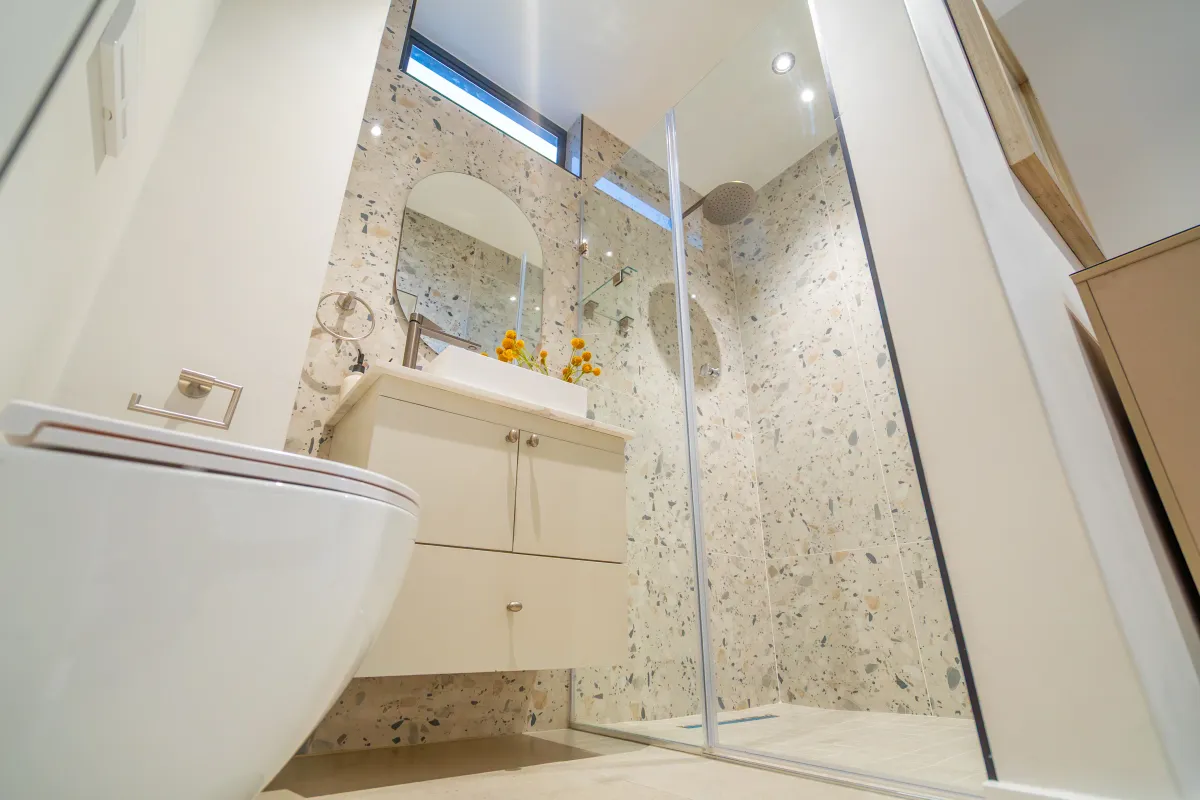 Modern bathroom featuring a wall-mounted toilet, floating vanity with vessel sink, and a spacious glass-enclosed shower with stylish terrazzo-style wall tiling.