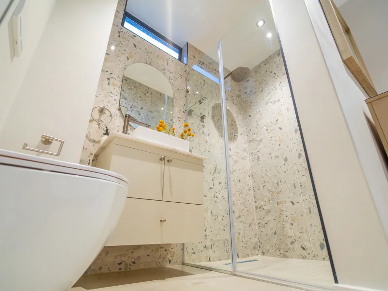 Modern bathroom featuring a wall-mounted toilet, floating vanity with vessel sink, and a spacious glass-enclosed shower with stylish terrazzo-style wall tiling.