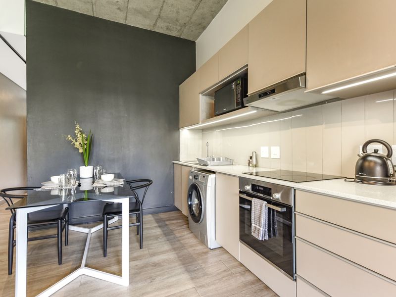 Modern open-plan kitchen featuring sleek cabinetry, integrated appliances, stone countertops, and an exposed concrete ceiling, seamlessly flowing into the dining area.