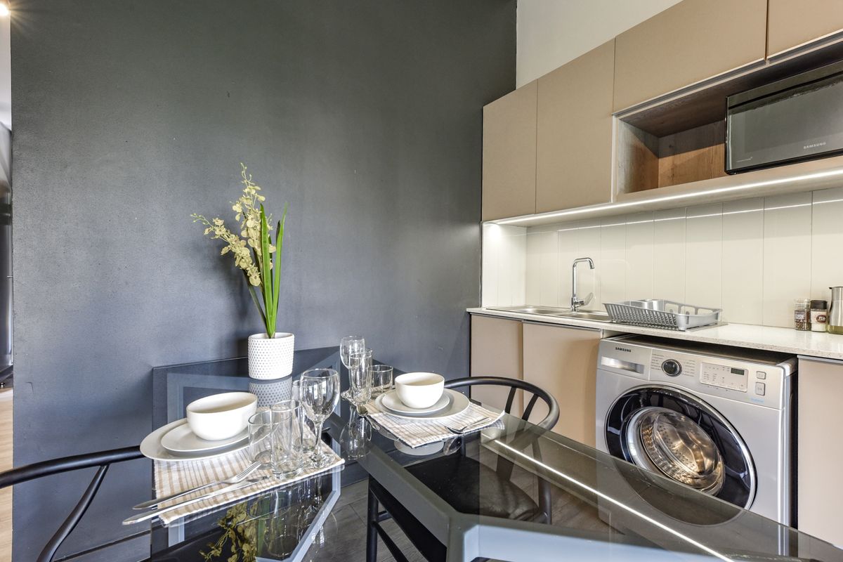 Modern compact kitchen featuring sleek beige cabinetry, integrated appliances, under-cabinet lighting, and a functional stone countertop workspace.