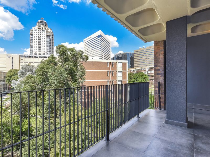 A modern, well-maintained balcony featuring tiled flooring, a sleek metal balustrade, and an exposed concrete ceiling, offering expansive urban city views.