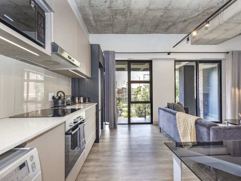 Modern open-plan kitchen and living area featuring an exposed concrete ceiling, sleek cabinetry, high-end built-in appliances, and large sliding doors leading to a balcony.