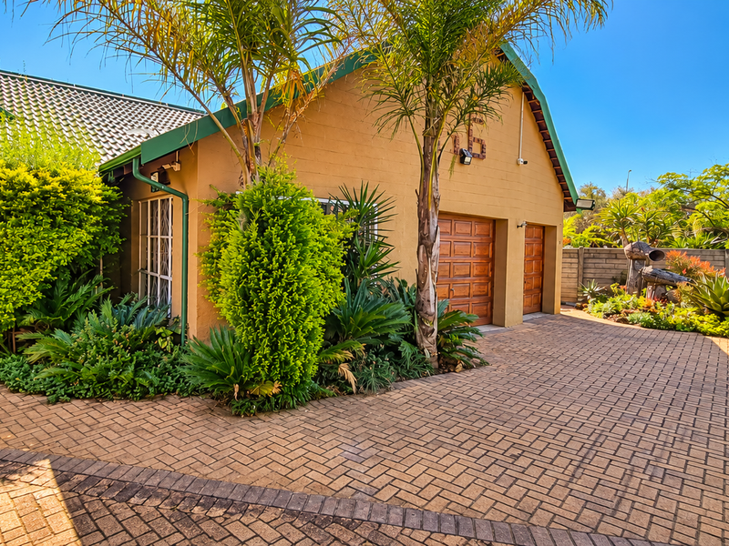 Front elevation of a house featuring a paved driveway, double garage, and established garden landscaping with a secure perimeter fence.