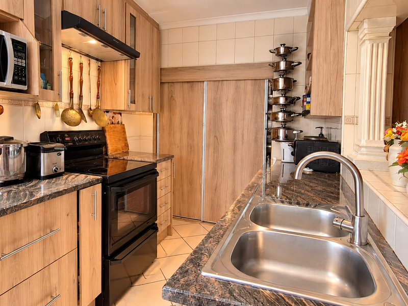 A functional kitchen featuring wood-look cabinetry, granite countertops, a double basin sink, and integrated appliances including a stove and microwave.