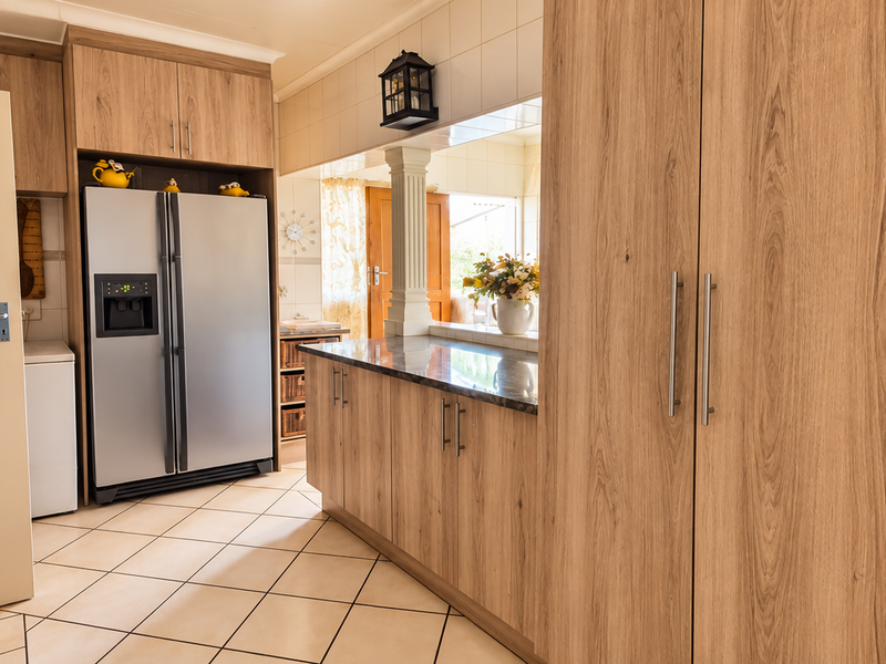 A functional kitchen featuring wood-look laminate cabinetry, stone-effect countertops, tiled flooring, and a convenient pass-through window connecting to the adjacent living space.