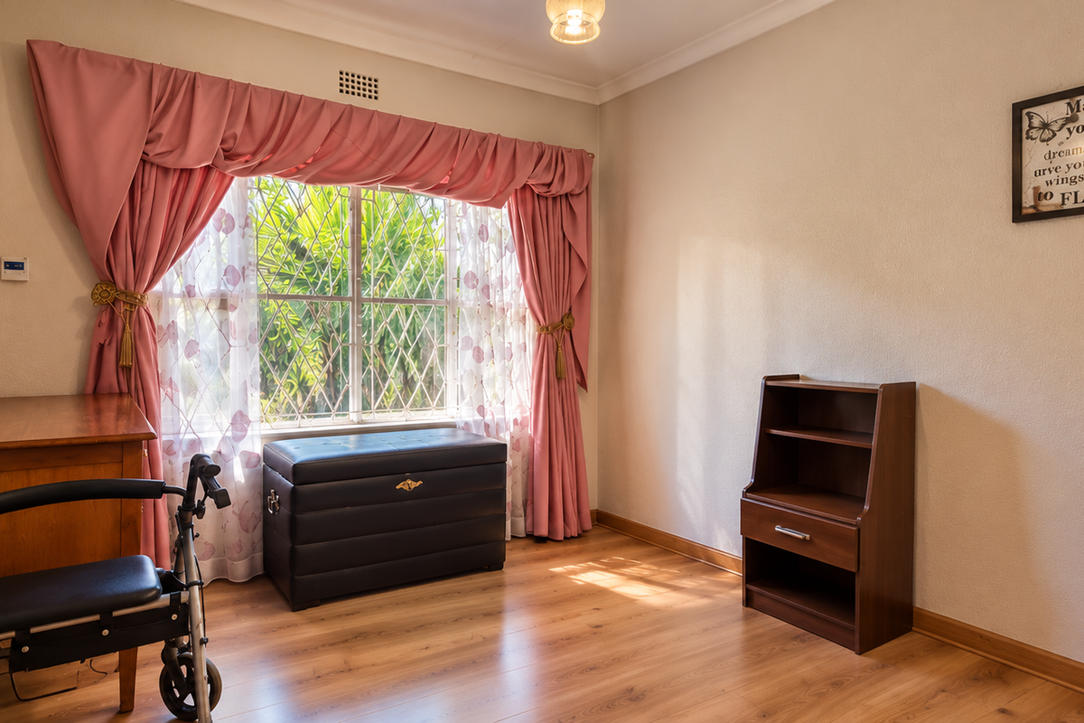 A bedroom featuring laminate flooring, a built-in cupboard, and a window fitted with security bars, offering a functional and well-lit living space.