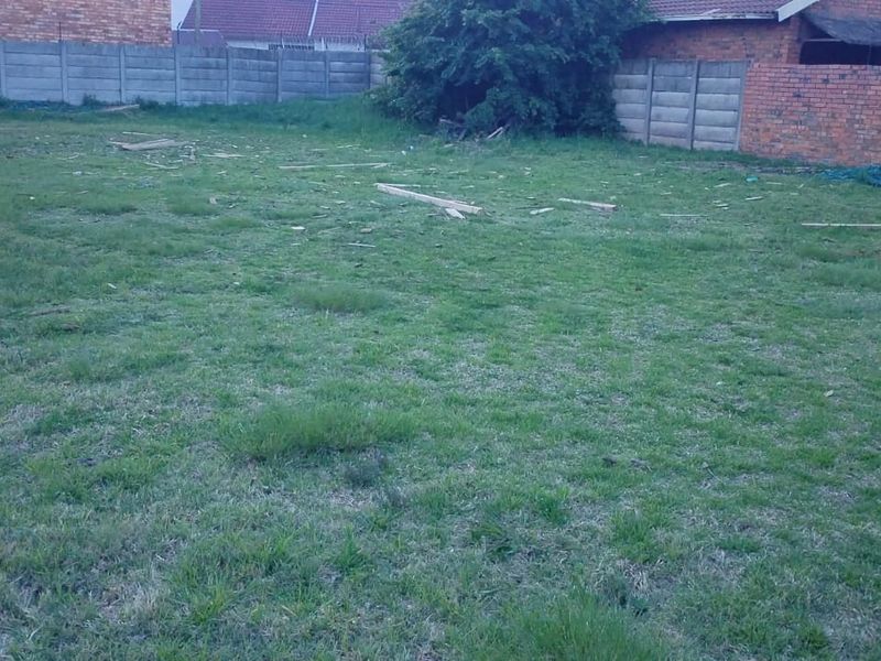 A vacant residential plot featuring grass coverage and enclosed by a combination of precast concrete and brick boundary walls.