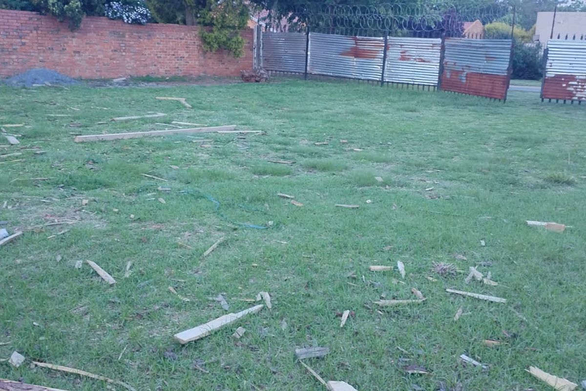 A vacant residential plot featuring a grassed area enclosed by a brick boundary wall and corrugated metal fencing with razor wire.