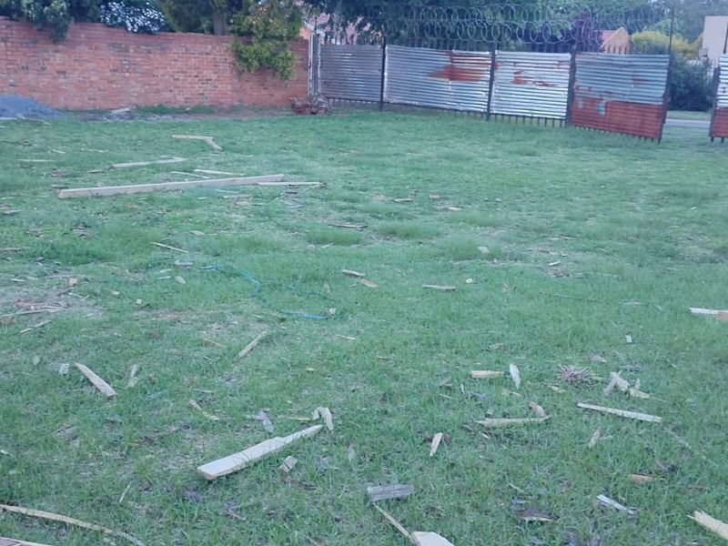 A vacant residential plot featuring a grassed area enclosed by a brick boundary wall and corrugated metal fencing with razor wire.