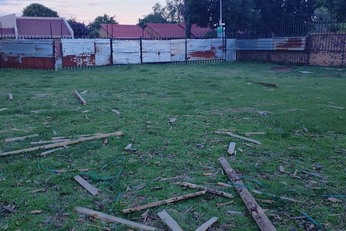 A vacant residential plot featuring a grass lawn enclosed by a combination of corrugated metal fencing and brick boundary walls.