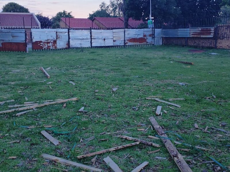 A vacant residential plot featuring a grass lawn enclosed by a combination of corrugated metal fencing and brick boundary walls.