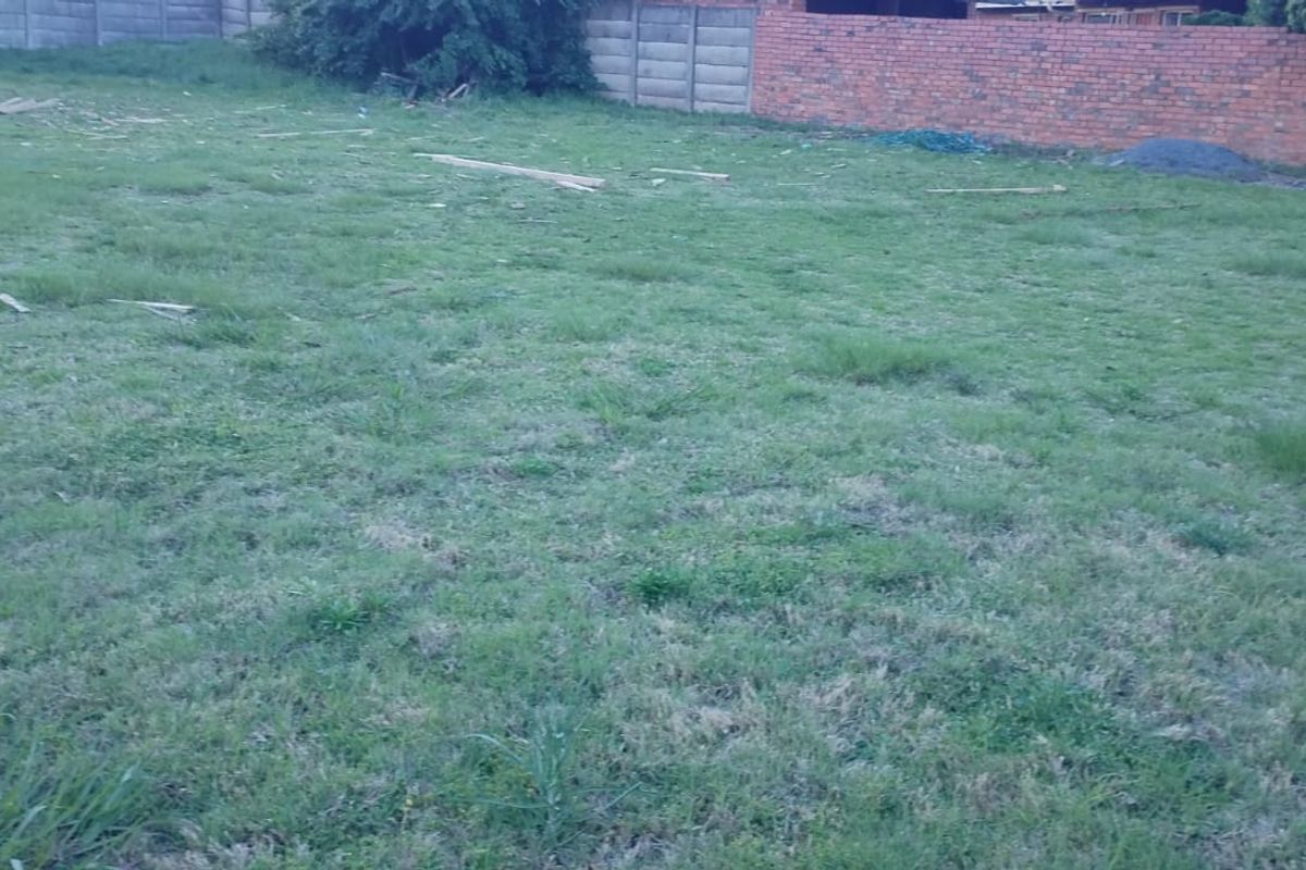A vacant residential plot featuring grass coverage and established brick and precast concrete boundary walls.